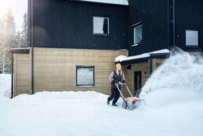 En person rydder snø foran et hus med en Husqvarna ST 253i.