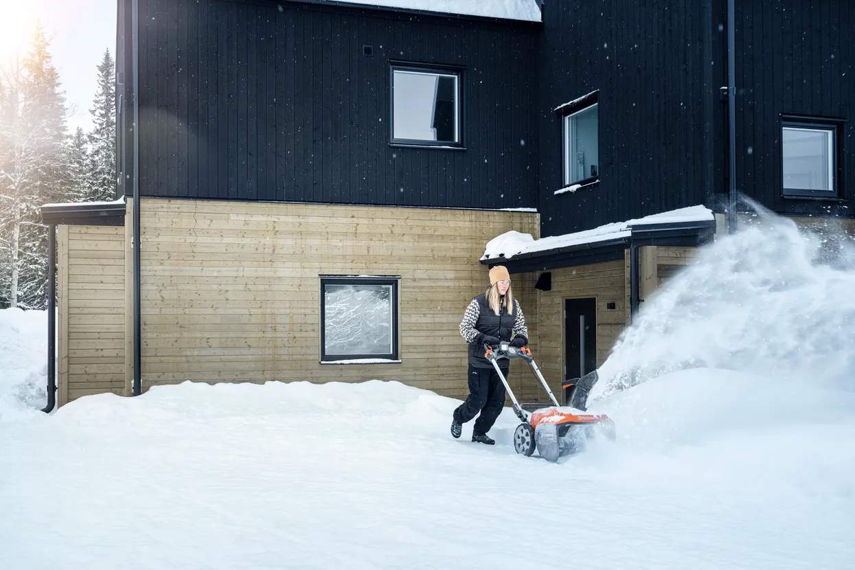 En person rydder snø foran et hus med en Husqvarna ST 253i.